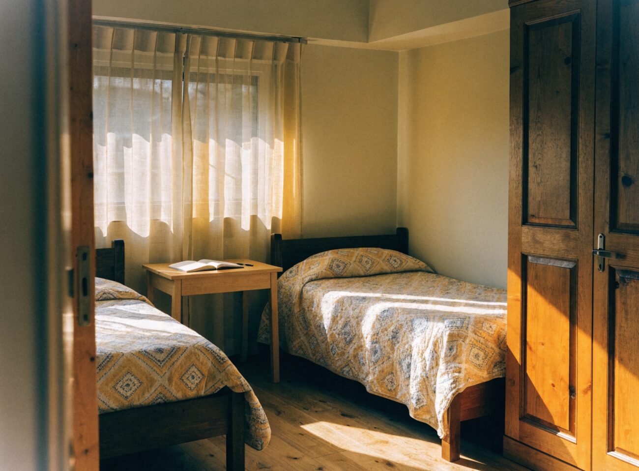 A sunlit shared bedroom in a sober living home with two neatly made beds and an open notebook on the table
